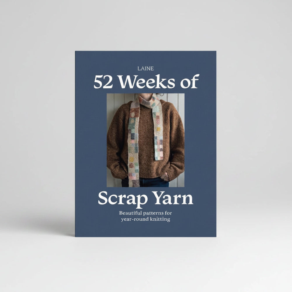 The front cover of the knitting book 'Laine 52 Weeks of Scrap Yarn' by Laine, featuring a dark slate blue background with white text and a central photograph of a person wearing a knitted brown sweater and a colorful patchwork scarf.