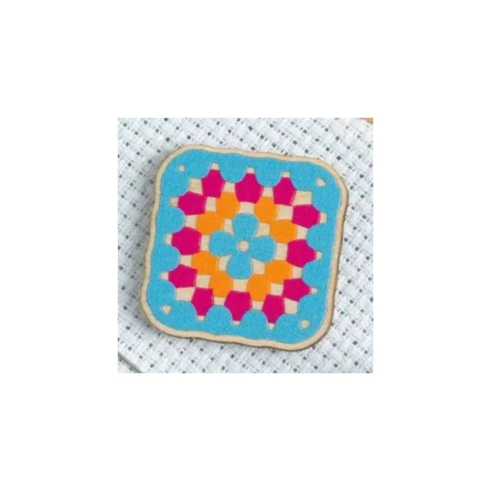 A square fabric patch with rounded corners featuring a colorful geometric granny square pattern, displayed on a white textured mesh background.