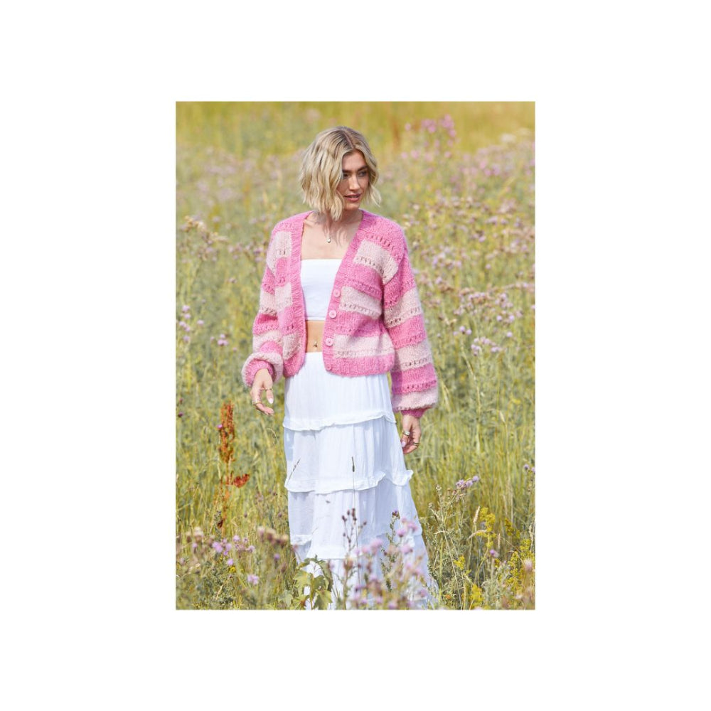 A woman standing in a field of wildflowers, wearing a pink and white striped knit cardigan over a white dress.