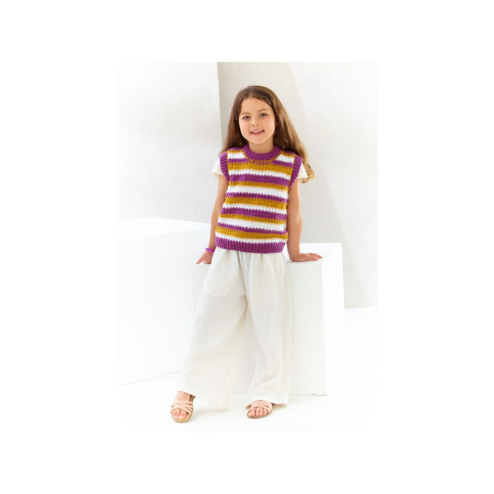 A young girl modeling a hand-knit short-sleeve top with purple, yellow, and white horizontal stripes, paired with white wide-leg pants and sandals, standing against a white geometric background.