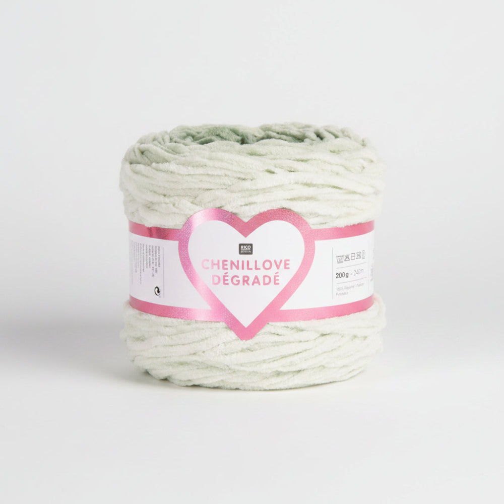 A roll of Chenillové Dégradé yarn in a soft mint green color, wrapped with a pink and white paper label featuring a glittery heart.