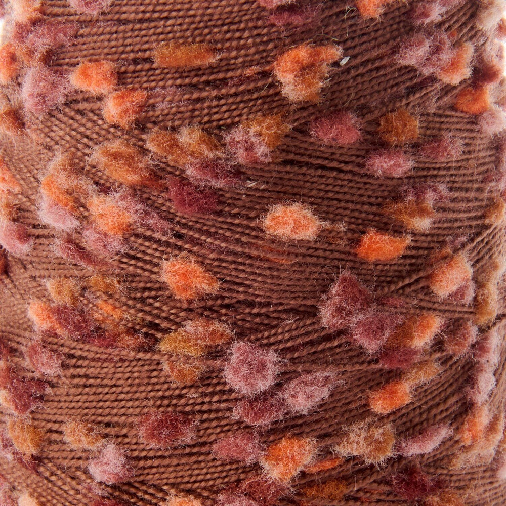 Close-up of a brown yarn ball with textured, fuzzy orange and dusty rose pom-pom accents.