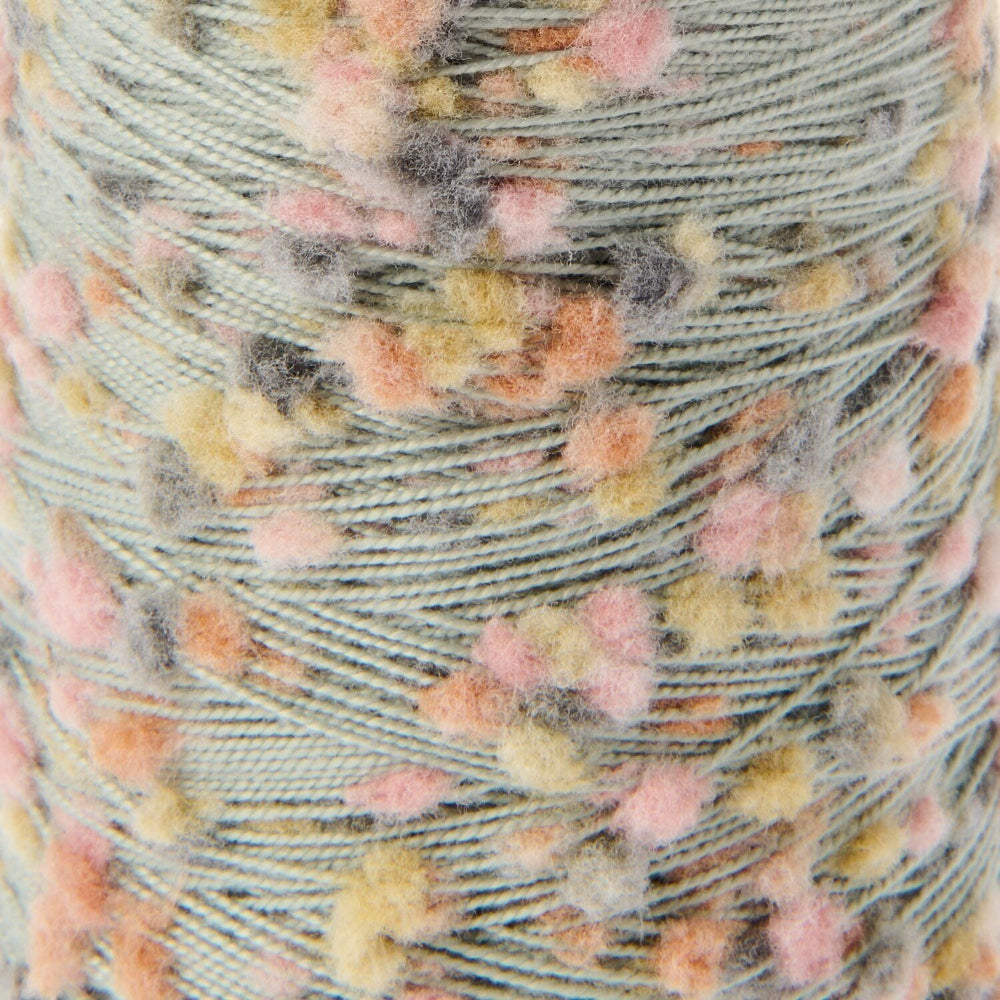 Close-up of a wound spool of variegated yarn with a sage green base and fuzzy pom-pom accents in pink, peach, yellow, and gray.