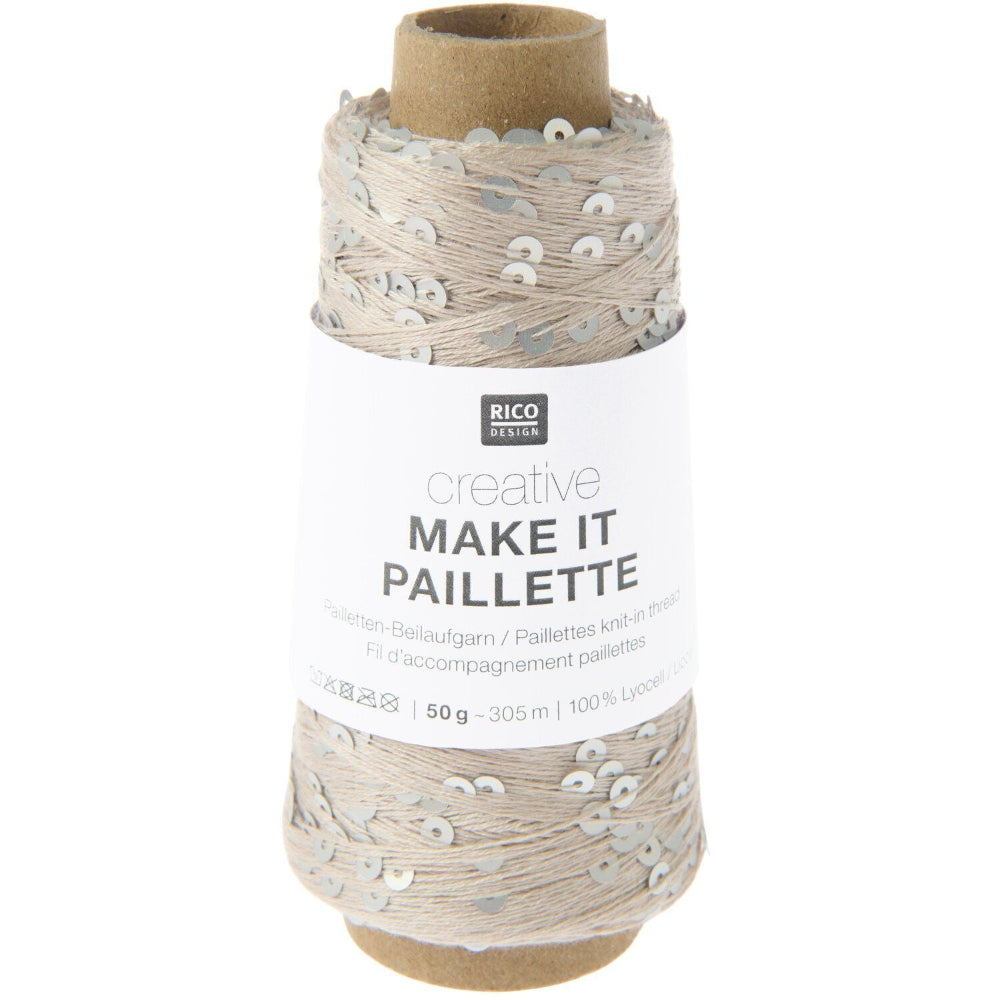 A spool of Rico Design Creative Make It Pailleçte yarn thread, featuring a white paper label with black text and silver sequins on a light beige thread wound around a brown cardboard core, set against a plain white background.