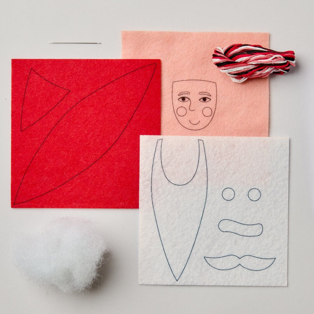 DIY felt crafting kit with red and white felt sheets, embroidered facial templates, white stuffing ball, and red-and-white striped thread on a light grey background.