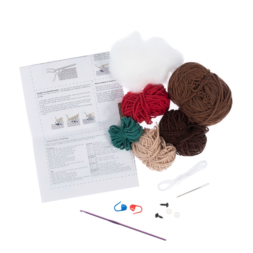 A crochet kit laid out on a white background, including a printed instruction sheet, yarn balls in white, red, green, beige, and brown, a purple crochet hook, knitting needles, stitch markers, and other small accessories.