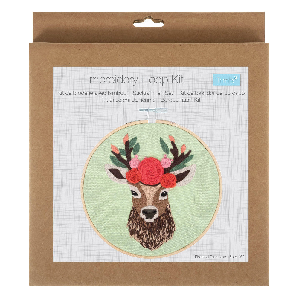 An embroidery hoop kit in its original brown kraft paper packaging, featuring a printed illustration of a deer with a floral crown on a light green background.