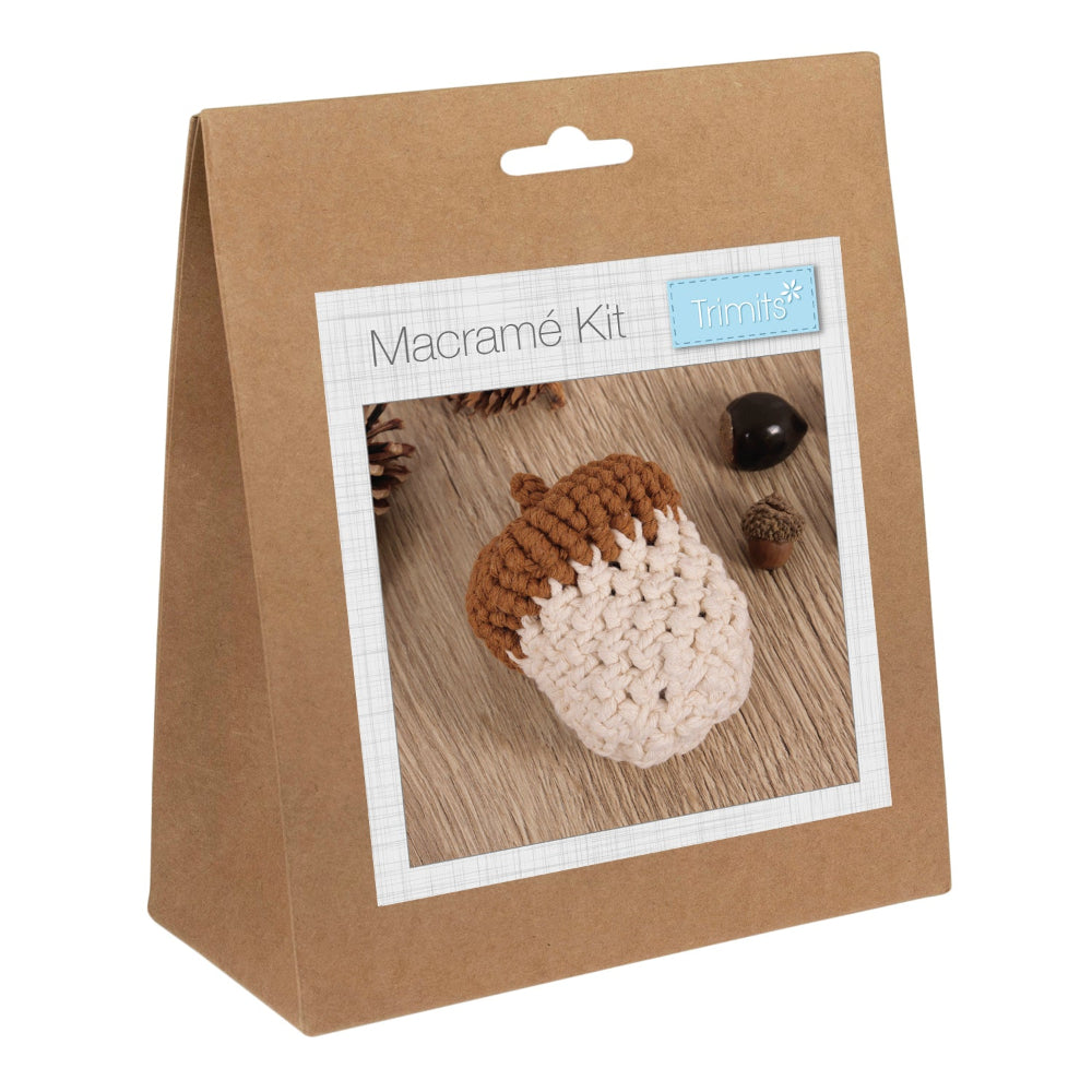 A brown kraft paper hanging bag package labeled 'Macramé Kit' with a small 'Trimits' logo, shown on a plain white background. The front has a photo window displaying a macrame acorn in brown and cream.