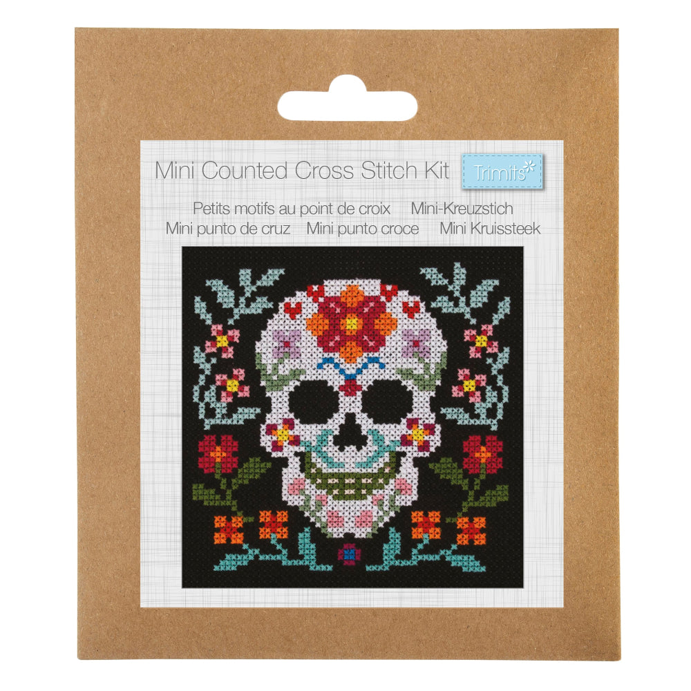 A Mini Counted Cross Stitch Kit by Trimits, featuring a sugar skull design on a black background with colourful floral details, presented in its brown cardboard packaging with a white label insert.