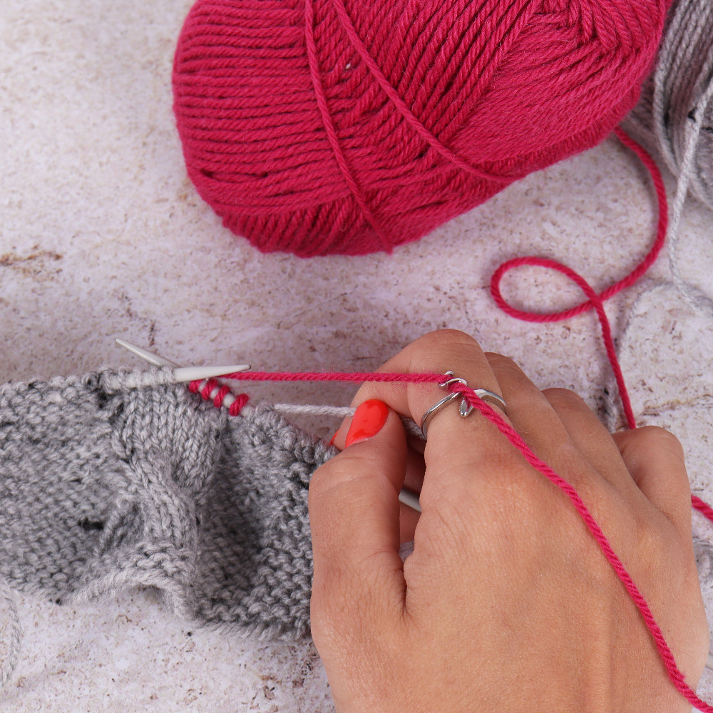 Person knitting with red yarn and grey fabric on a light surface