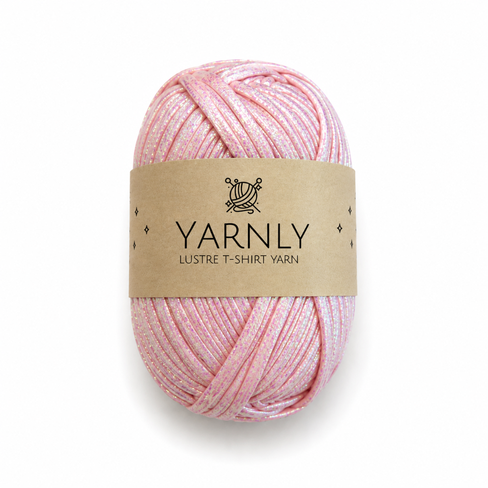A skein of Yarnly Lustre T-Shirt Yarn in a soft pink color with subtle shimmer, wrapped in a brown paper label, on a white background.