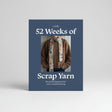 The front cover of the knitting book 'Laine 52 Weeks of Scrap Yarn' by Laine, featuring a dark slate blue background with white text and a central photograph of a person wearing a knitted brown sweater and a colorful patchwork scarf.