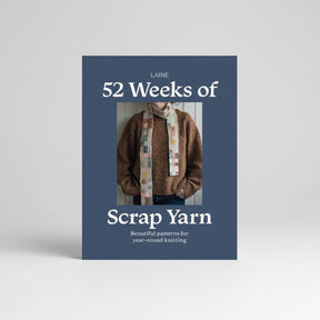 The front cover of the knitting book 'Laine 52 Weeks of Scrap Yarn' by Laine, featuring a dark slate blue background with white text and a central photograph of a person wearing a knitted brown sweater and a colorful patchwork scarf.