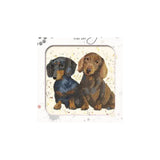 A diamond painting or craft kit featuring an illustration of two dachshunds, one black and tan and one brown, on a speckled cream background. The package has a white border with 'FINE ART' printed at the top.