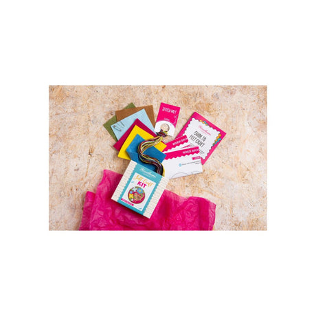 A flat-lay of colourful craft supplies fanned out above a bright pink tissue paper on a textured beige surface.