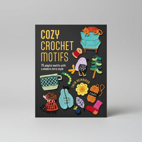 The front cover of the book 'Cozy Crochet Motifs' by Julia Rehnberg, featuring a dark charcoal background with yellow title text and multiple colorful crocheted-style motifs including a turquoise armchair, orange cat, pink sweater, green tree, and other autumn and cozy elements.