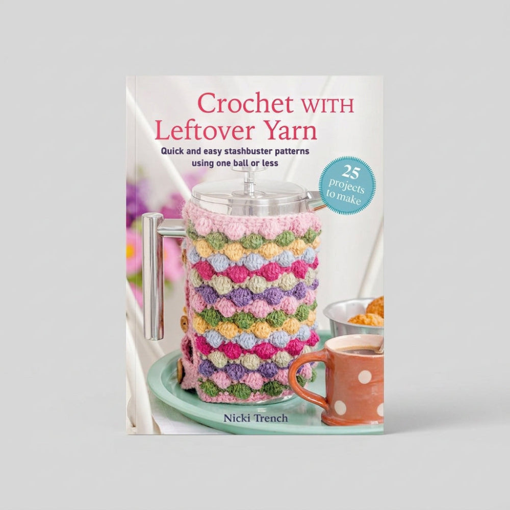 Crochet with Leftover Yarn book by Nicki Trench, featuring a colourful crocheted stasher cover on a teapot, with a pink polka-dot mug and a blue badge indicating 25 projects to make.
