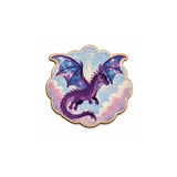 A scalloped-edge wooden pin or badge featuring a purple dragon with galaxy-patterned wings against a pastel sky background, shown on a plain white background.