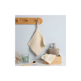 A cream-colored knitted dishcloth hanging from a wooden peg on a light blue-grey wall, with a matching folded dishcloth and soap dispenser in a wooden tray on a white countertop.