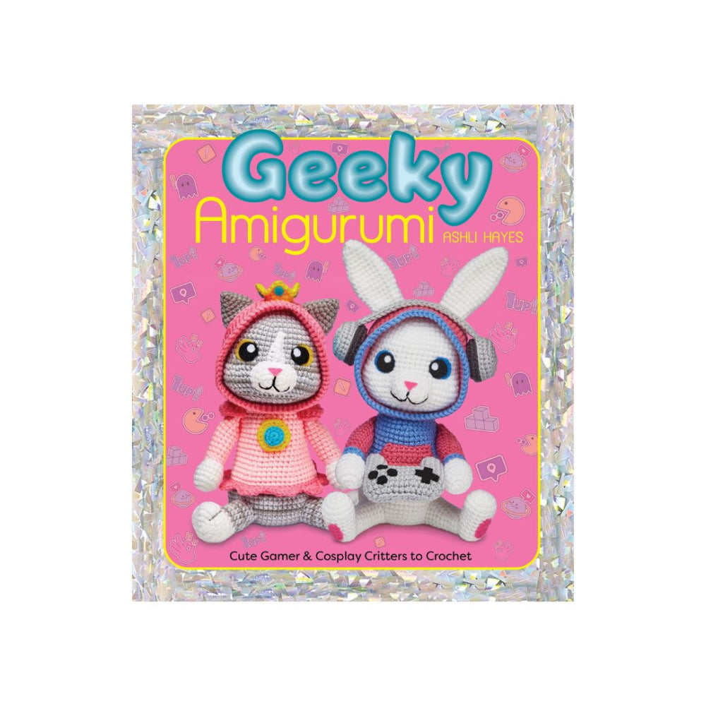Front cover of a crochet book titled "Geeky Amigurumi" showing two crocheted character figures: a cat in a pink hood with a small crown and a bunny in a blue-and-pink hood with headphones. The cover has a pink background with a glittery silver border.