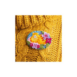 An oval embroidered patch featuring a yellow cat surrounded by pink and purple flowers on a blue background, displayed on a yellow cable-knit sweater against a white backdrop.