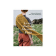 Book cover for 'Grand Shetland Adventure Knits' by Gudrun Johnston & Mary Jane Mucklestone, showing a person outdoors wearing and draping a mustard yellow knitted shawl over grassy ground.