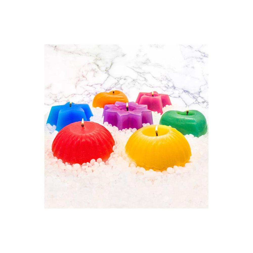 A set of colourful wax candles shaped like fruits and flowers, including red, yellow, green, blue, orange, pink, and purple candles, arranged in white wax beads on a white marble surface.
