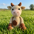 Crocheted toy cow with brown accents on a field background