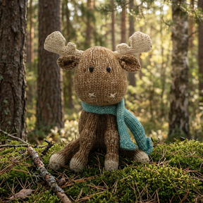 A knitted moose toy with brown and beige knit body, cream-colored antlers and hooves, and a teal knit scarf