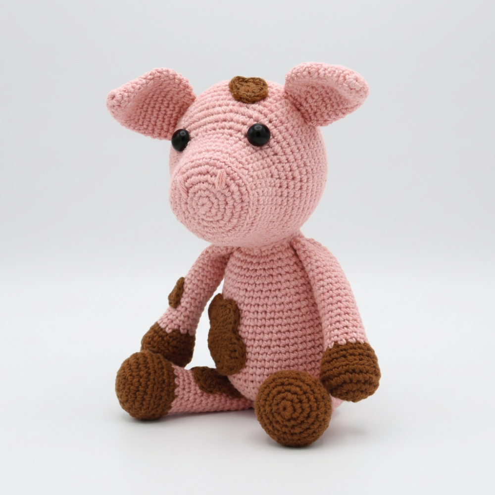 Crocheted pink pig toy with brown accents on a white background