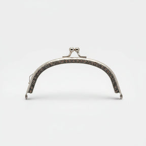 A silver metal bag clasp with clear rhinestones, presented in its pink retail packaging by Hemline.