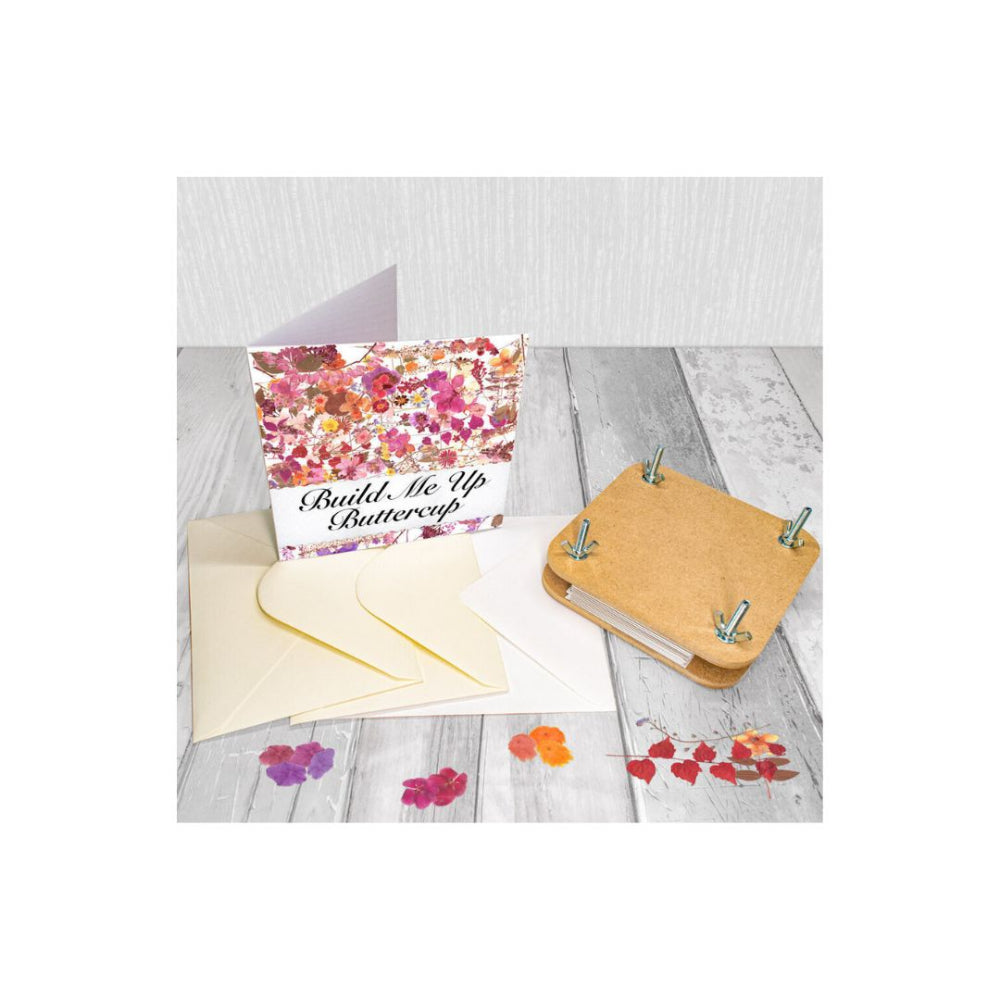 A flower-themed card set displayed on a light grey wood surface, including a floral  card, cream envelopes, and a small cork binder with butterfly wings and metal clips.