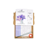 An origami kit in a brown cardboard box, featuring a printed paper template for 'Origami Flowers' with purple and pink lilies, practice sheets, green stems, and a small orange roll, all photographed on a white background.