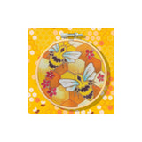 A round embroidery hoop containing a floral bee design on a yellow honeycomb-patterned fabric, shown against a matching yellow patterned background.
