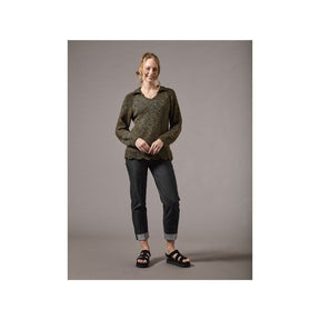 A woman modeling a dark olive green and black patterned knit sweater, paired with dark gray cuffed jeans and black sandals, standing against a solid gray studio background.