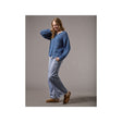 A woman modeling a blue textured knit cardigan sweater, light-wash wide-leg jeans, and brown suede mules against a solid gray studio background.