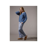 A woman modeling a blue textured knit cardigan sweater, light-wash wide-leg jeans, and brown suede mules against a solid gray studio background.