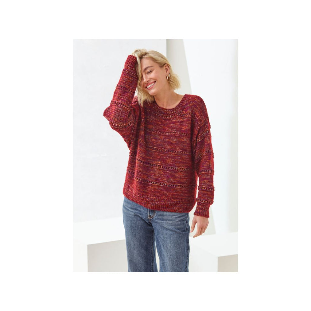 A woman wearing a marled red and orange knit sweater with blue jeans, standing against a clean white background.