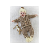 A baby lying on a textured white blanket wearing a knitted one-piece outfit in brown and cream, with a matching cream knit hat and a small stuffed bunny toy.