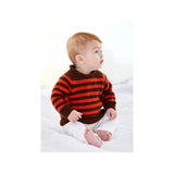 A baby sitting on a white bed wearing a brown and orange striped knit sweater and white pants.