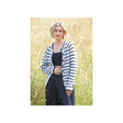 A woman standing in a sunlit grassy field wearing a fuzzy black-and-white striped cardigan over a black outfit.
