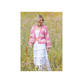 A woman standing in a field of wildflowers, wearing a pink and white striped knit cardigan over a white dress.