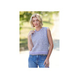 A woman wearing a lavender sleeveless knit sweater vest with a white geometric pattern, paired with blue jeans, standing outdoors against a blurred green background.