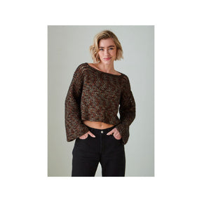 A woman modeling a cropped, long-sleeve crochet top with a brown and black textured pattern, paired with black jeans, against a solid light gray background.