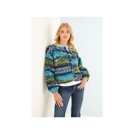 A woman modeling a multicolour crochet cardigan with horizontal stripes of blue, teal, green, and navy, paired with a white undershirt and dark blue jeans.