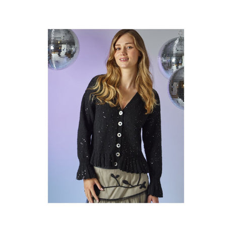 A woman modeling a black knit cardigan with white buttons, featuring a V-neck and ruffled cuffs, set against a lavender background with hanging disco ball decorations.