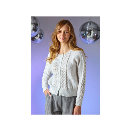 A woman modeling a light grey cable-knit cardigan sweater with grey trousers, standing against a purple-lit background with two hanging disco balls.