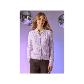 A woman wearing a light purple lace cardigan with button-front closure, paired with dark brown trousers, standing against a lavender studio backdrop with mirrored disco ball props.
