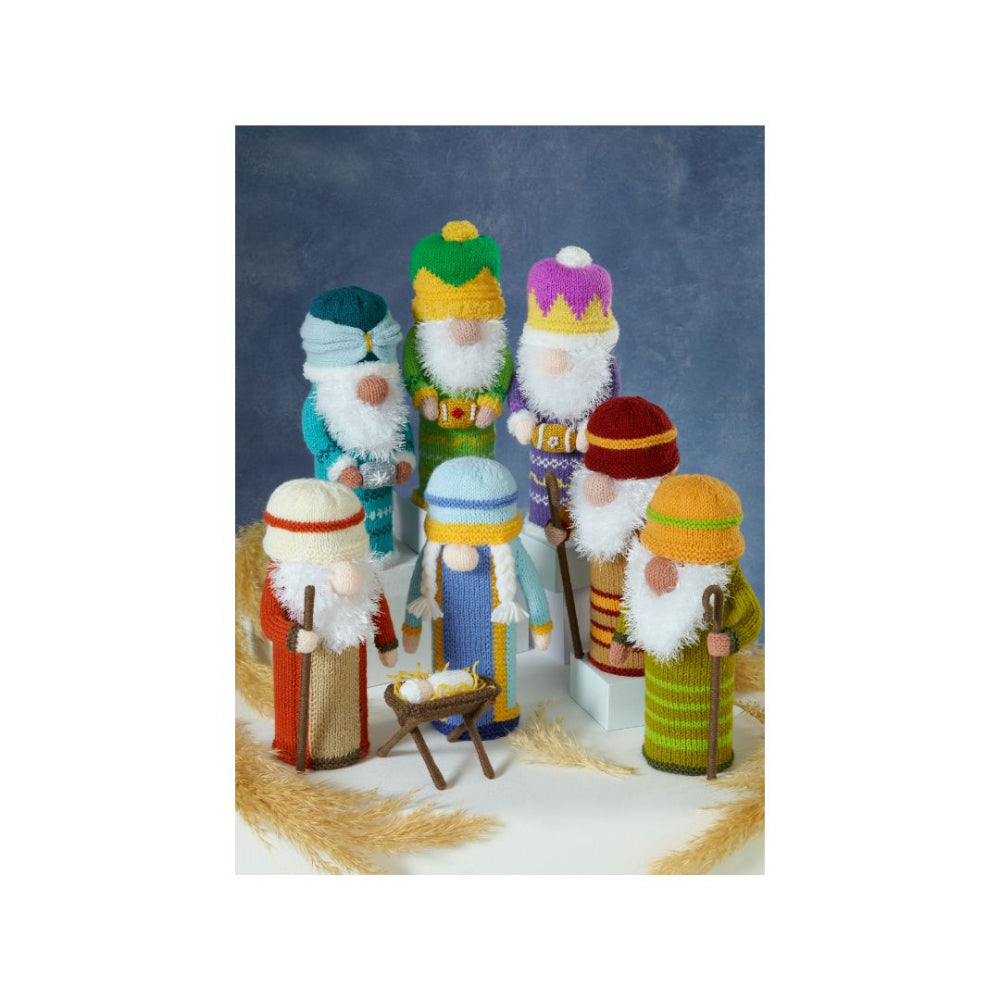 A set of hand-knit Christmas nativity figurines , featuring various wise men and a baby in a manger, arranged on a white surface with decorative wheat against a blue background.