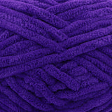 A close-up of thick, plush purple yarn strands arranged in a textured pattern.